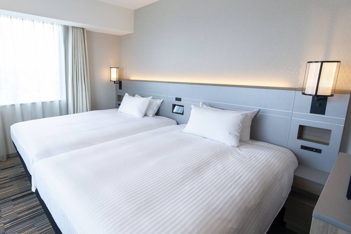 A hotel room with two beds, a desk, and a chair.