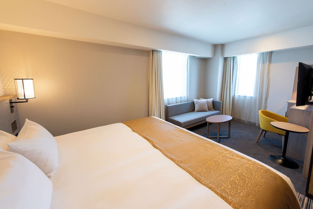 A hotel room with a large bed, a sofa, a small round table, and a TV.