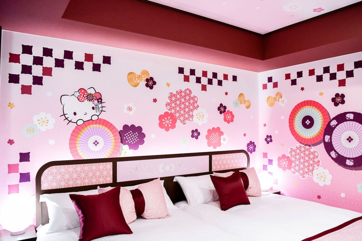 A bedroom with a bed, pillows, and a wall decorated with Hello Kitty and floral patterns.