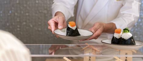A person in a white coat holding a plate with sushi.