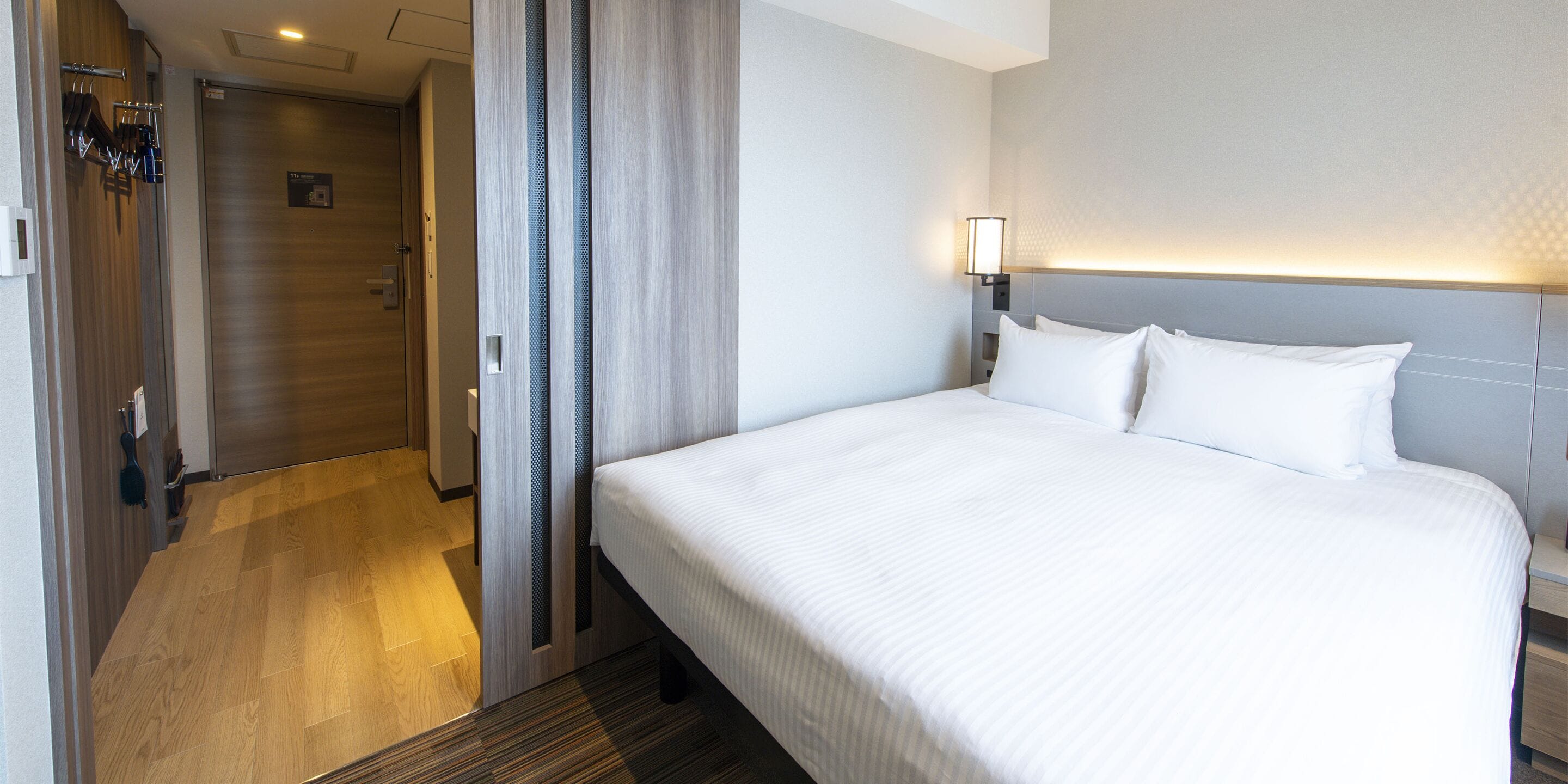 Una habitación de hotel con una cama grande, una mesita de noche, una lámpara y una puerta que da a un baño.