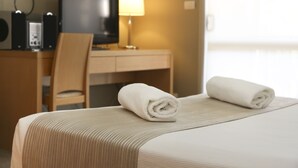 A hotel room with a bed, a desk with a computer, a chair, and a TV.