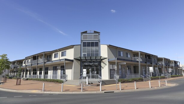 A multi-story building with a central entrance, balconies, and a clear sky.