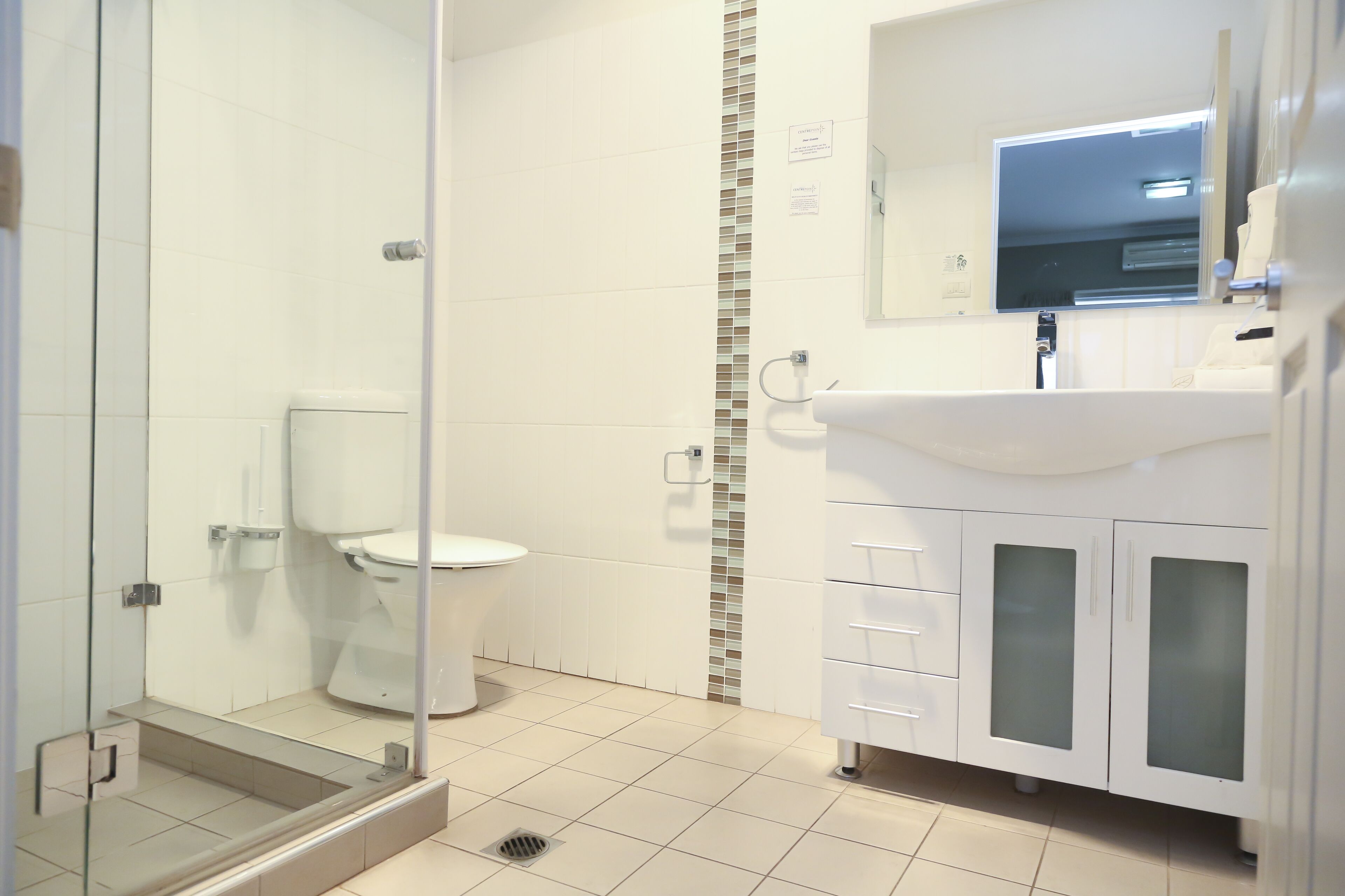 Un baño moderno con cabina de ducha de vidrio, inodoro blanco y tocador con puertas de vidrio esmerilado.