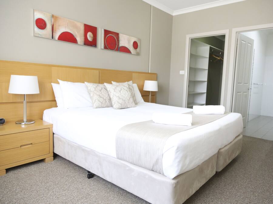 A neatly made bed with white linens, a wooden nightstand with a lamp, and a wall with abstract art.