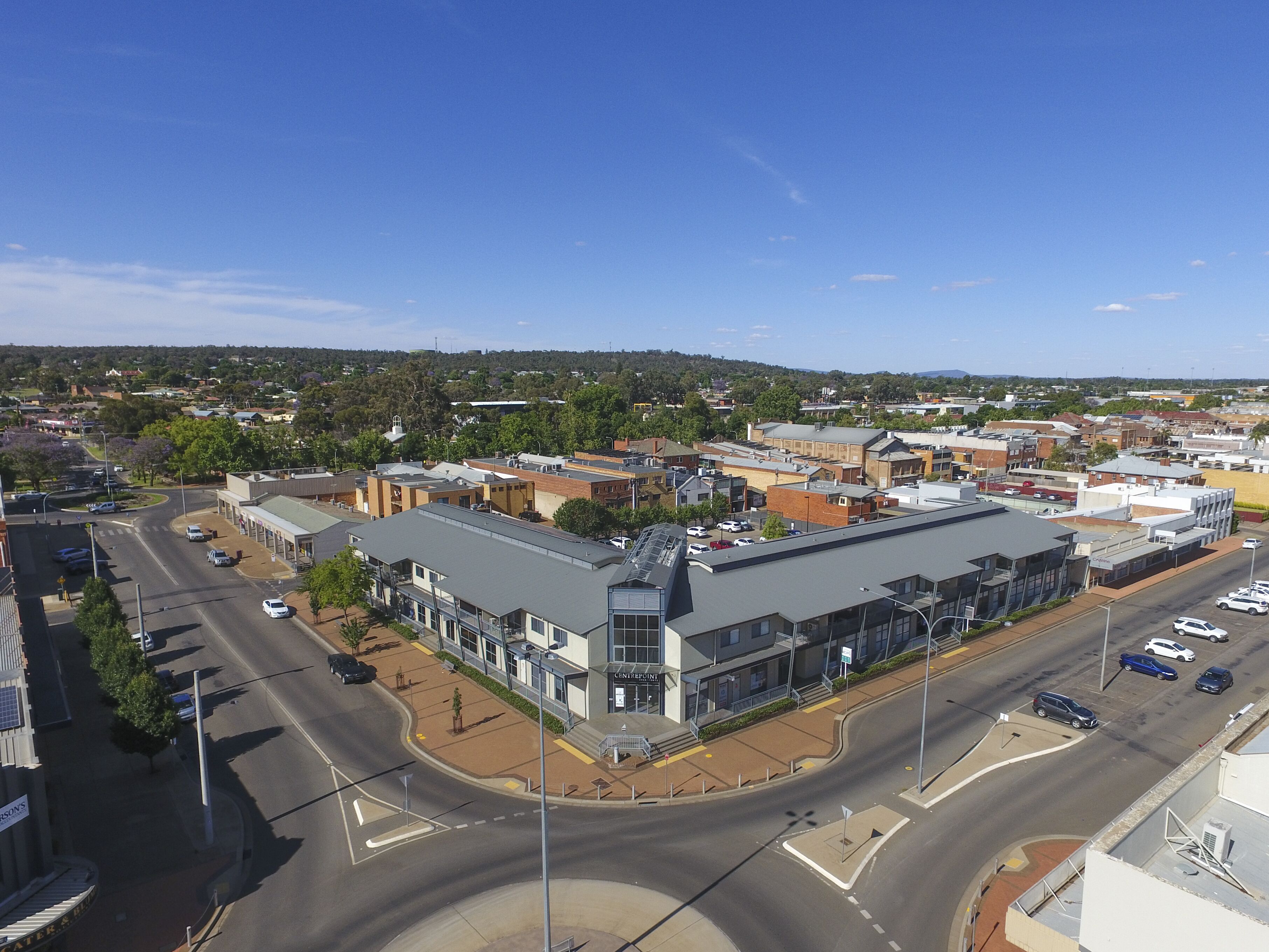 A multi-story building with a flat roof, a parking lot, and a street view.