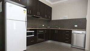 A modern kitchen with dark cabinets, a white refrigerator, a microwave, an oven, and a dishwasher.