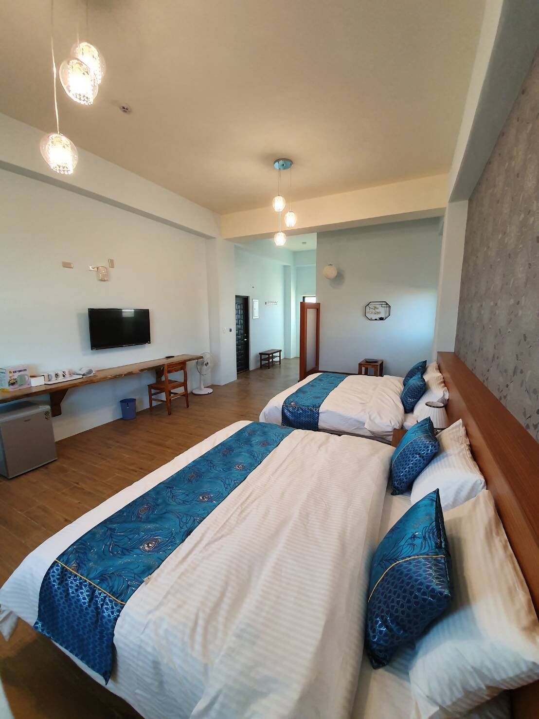 A hotel room with two beds, a desk, a television, and a small kitchenette.