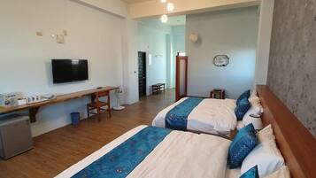 A hotel room with two beds, a desk, a television, and a small kitchenette.