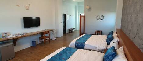 A hotel room with two beds, a desk, a television, and a small kitchenette.