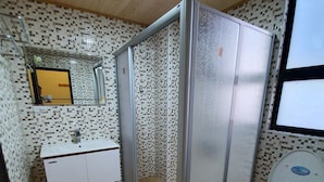 A bathroom with a shower enclosure, a toilet, a sink with a mirror, and tiled walls.