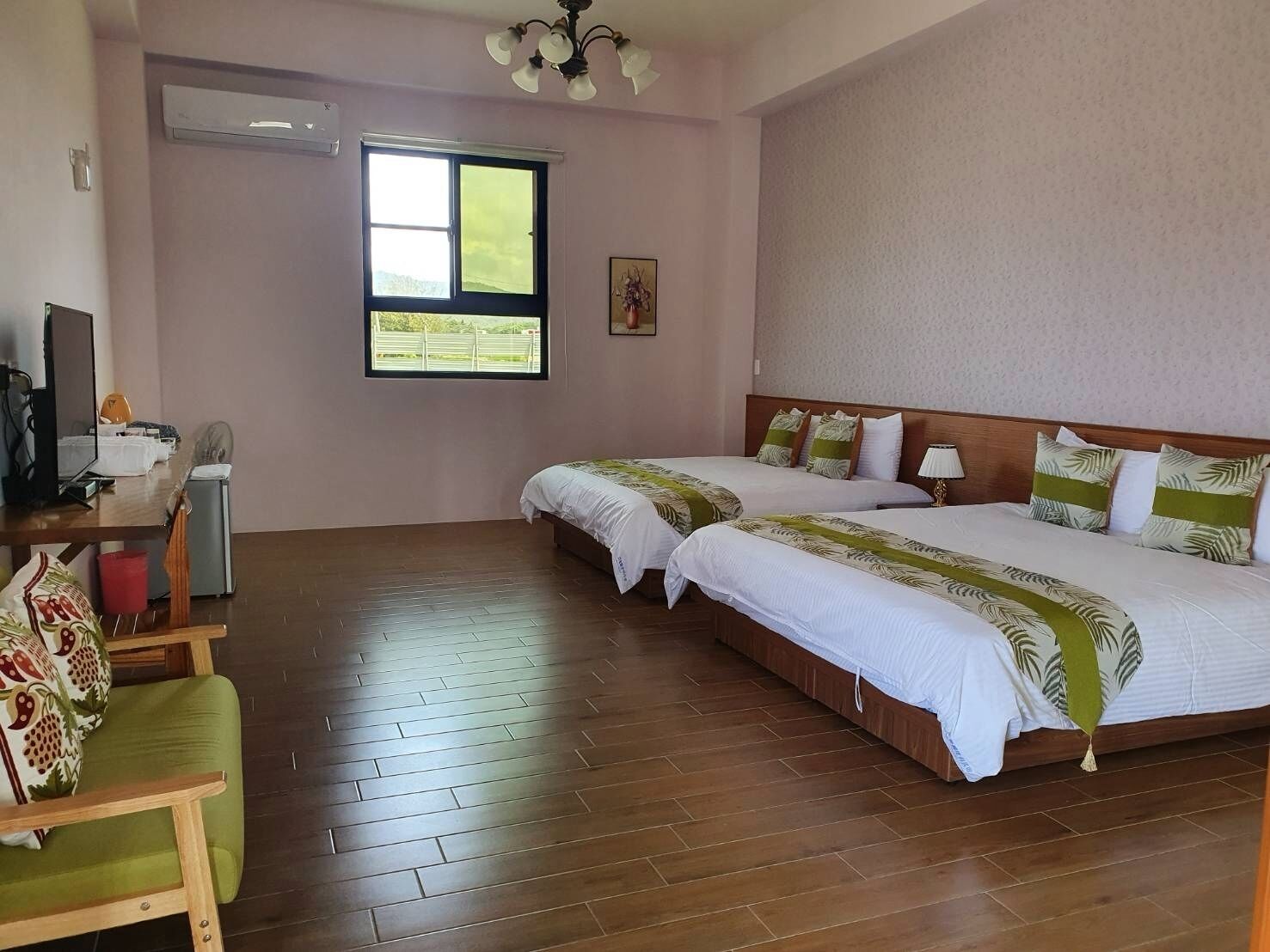 Habitación de hotel con dos camas, un escritorio con computadora, una silla y ventana con vista a áreas verdes.