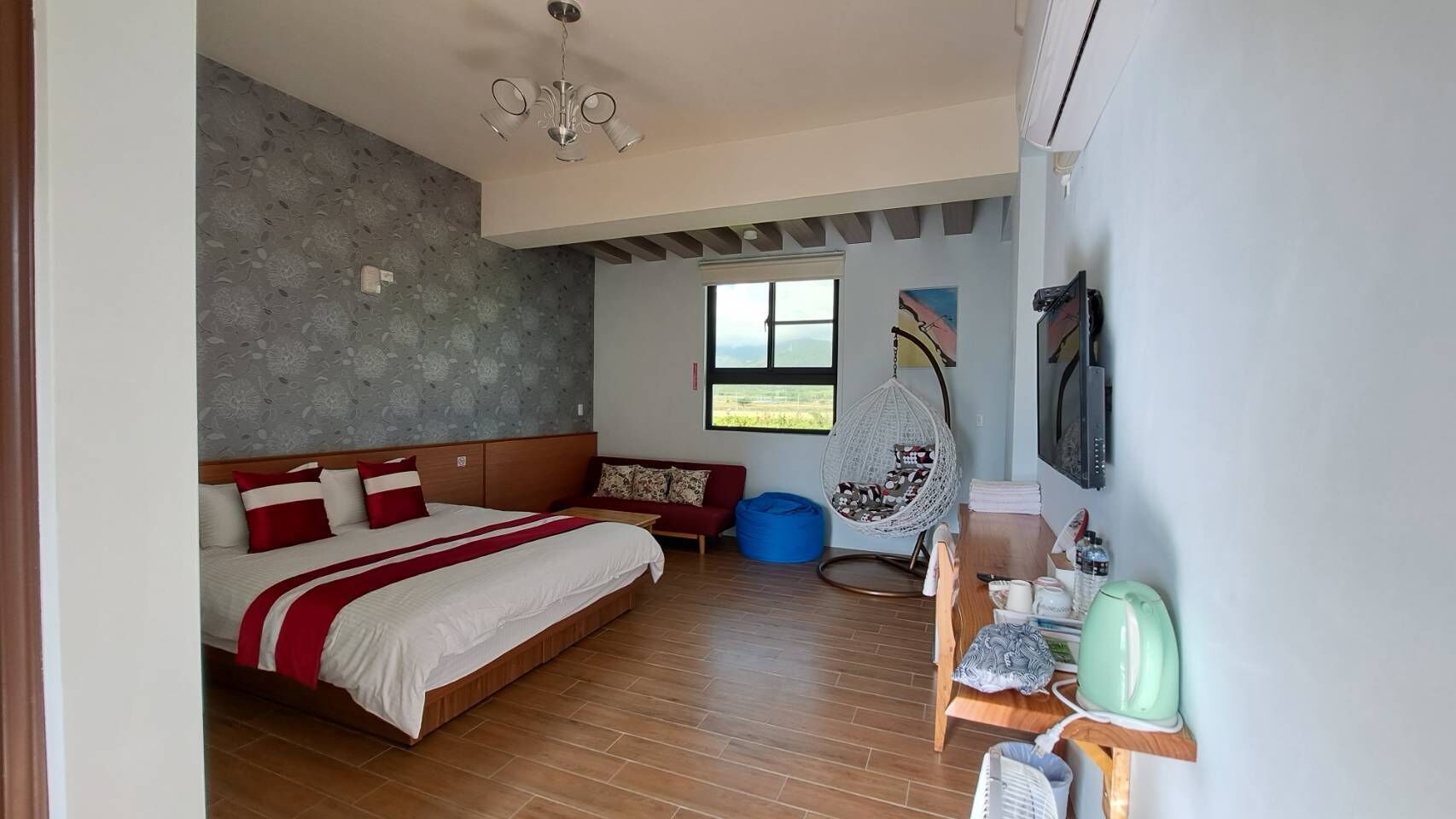A bedroom with a bed, a hanging chair, a sofa, a window, and a kitchenette area.