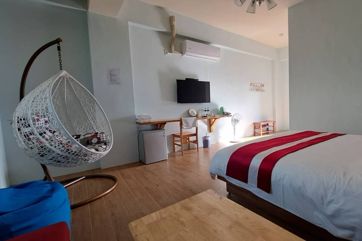 A bedroom with a bed, a hanging chair, a desk, and a television.