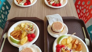 A dining table with plates of food, including sandwiches, potatoes, and salad. There are also condiments and a thermos on the table.