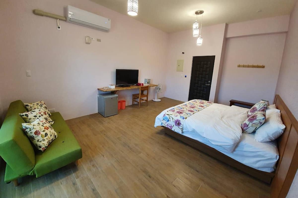 A room with a bed, a desk with a computer, a small fridge, a green sofa, and a TV.