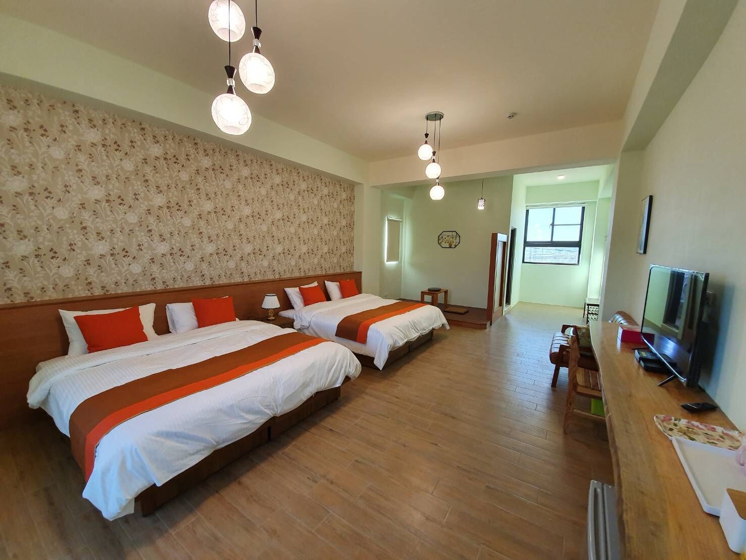A hotel room with two beds, wooden flooring, a TV, and a small table.