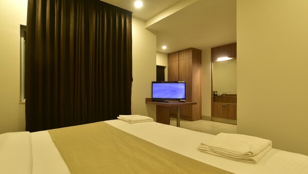 A hotel room with a bed, a television, a wooden cabinet, and a mirror. - Panchavati Express (Nashik)