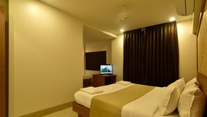 A hotel room with a bed, a TV, a nightstand, and a window with curtains. - Panchavati Express (Nashik)