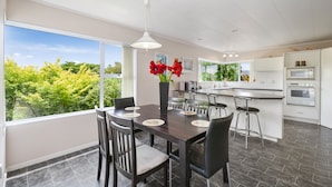 Une cuisine moderne dotée d’un grand îlot central, d’un revêtement de sol foncé et d’un coin repas avec des chaises et un vase de fleurs.