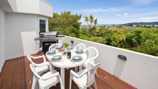 Une terrasse avec un barbecue, des chaises blanches et une table dressée pour le repas.