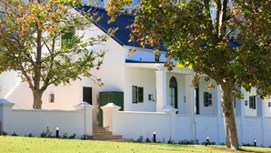 A white building with a blue roof, green shutters, and a well-maintained lawn. - La Cotte The Manor House (Franschhoek)