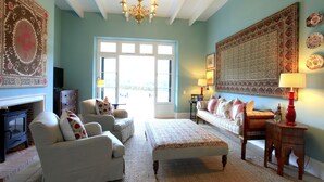 A cozy living room with a fireplace, a sofa set, a large rug, and a chandelier. - La Cotte The Manor House (Franschhoek)