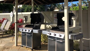 An outdoor barbecue area with two gas grills, a covered seating area, and a 'No Smoking' sign. - Princeville Delight! COLD A/C, Sleeps 4, Pool & Jacuzzi, Private Lanai & Space (Princeville)