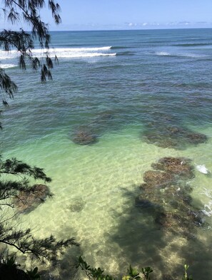 Vista despejada de una playa con aguas tranquilas y rocas visibles bajo la superficie.
