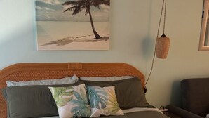 A bed with a green bedspread, multiple pillows, and a painting of a palm tree on the wall. - Princeville Delight! COLD A/C, Sleeps 4, Pool & Jacuzzi, Private Lanai & Space (Princeville)