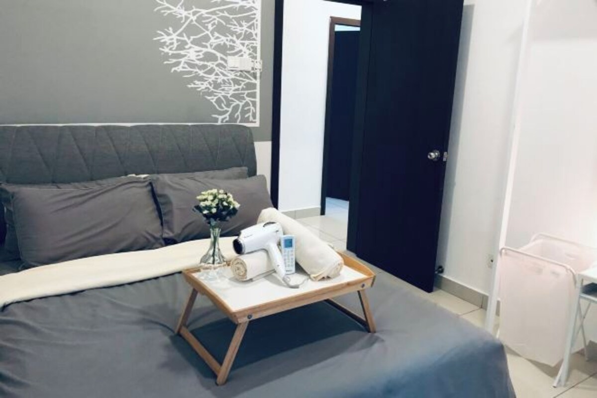 A neatly made bed with a grey comforter, a wooden tray with toiletries, and a wall art piece.