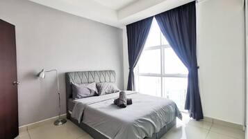 A modern bedroom with a large bed, a bedside lamp, and a view of the city through a window with curtains.