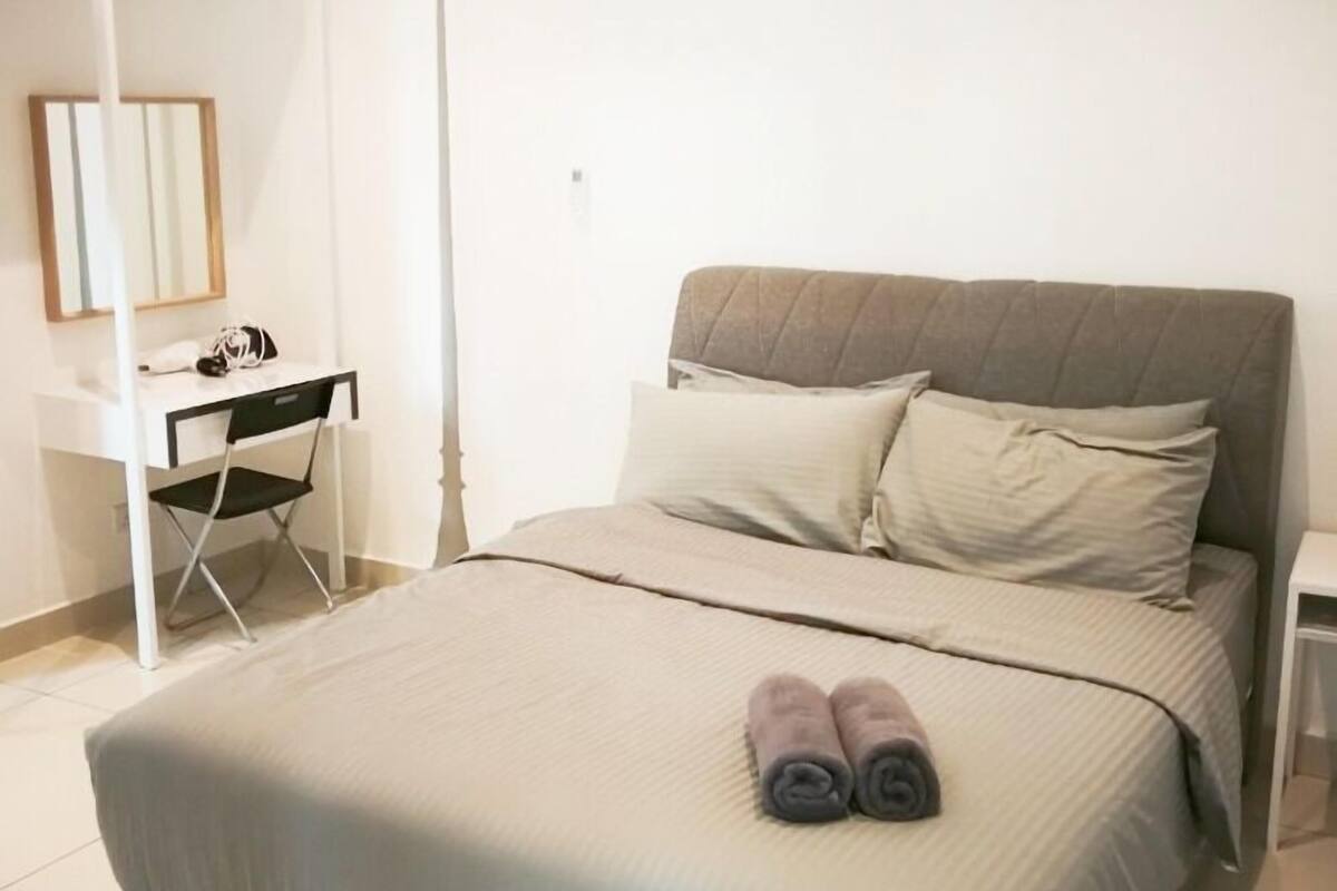 A bedroom with a bed, a desk, and a floor lamp.