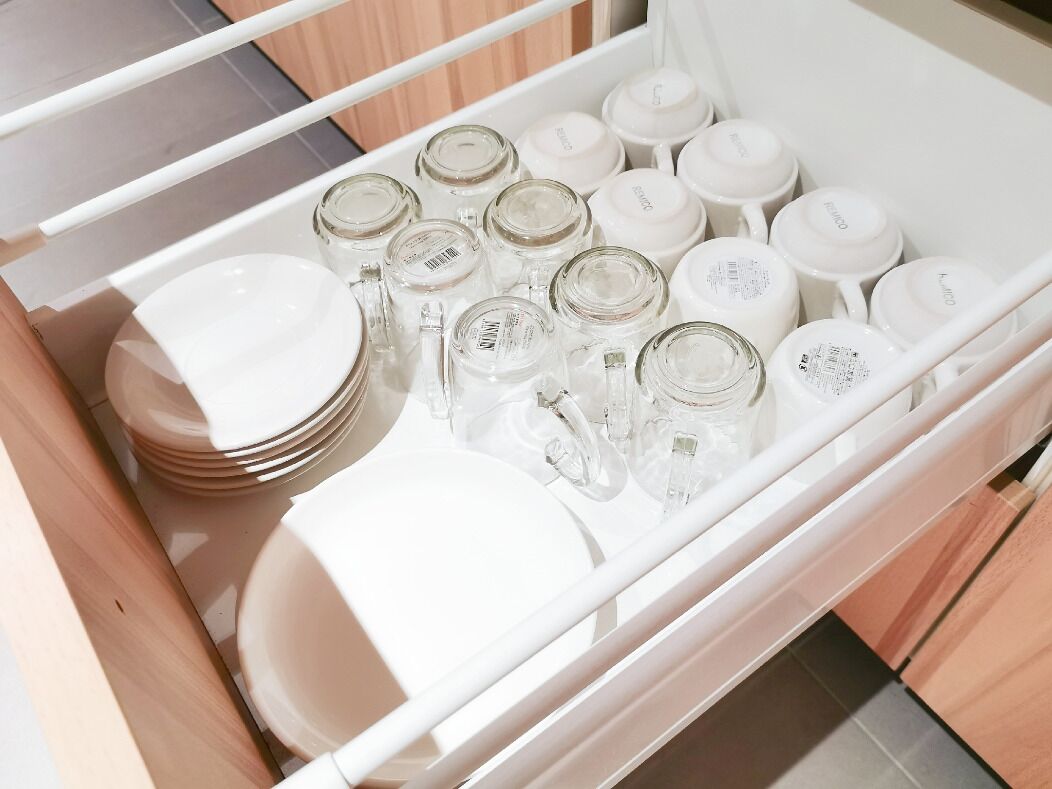A drawer containing white plates, bowls, and glass jars.