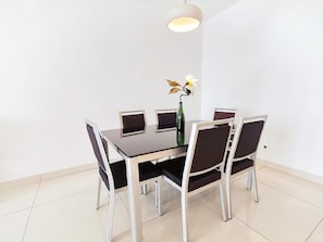 Uma sala de jantar com uma mesa retangular, seis cadeiras e um vaso com flores.