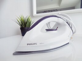 A Philips Affinity iron on a white surface with a potted plant beside it.