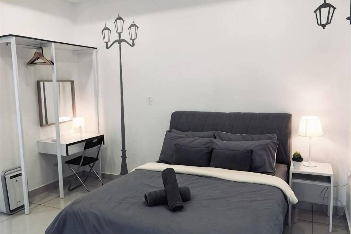 A bedroom with a bed, a desk, a chair, a wardrobe, and a nightstand with a lamp.
