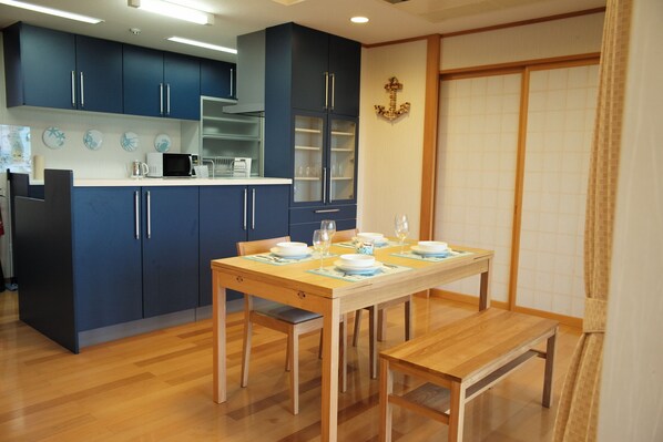 A modern kitchen with blue cabinets, a wooden dining table set for four, and a traditional sliding door in the background. - City 1500 SF 2BR condom 3F sea view (Ishigaki)