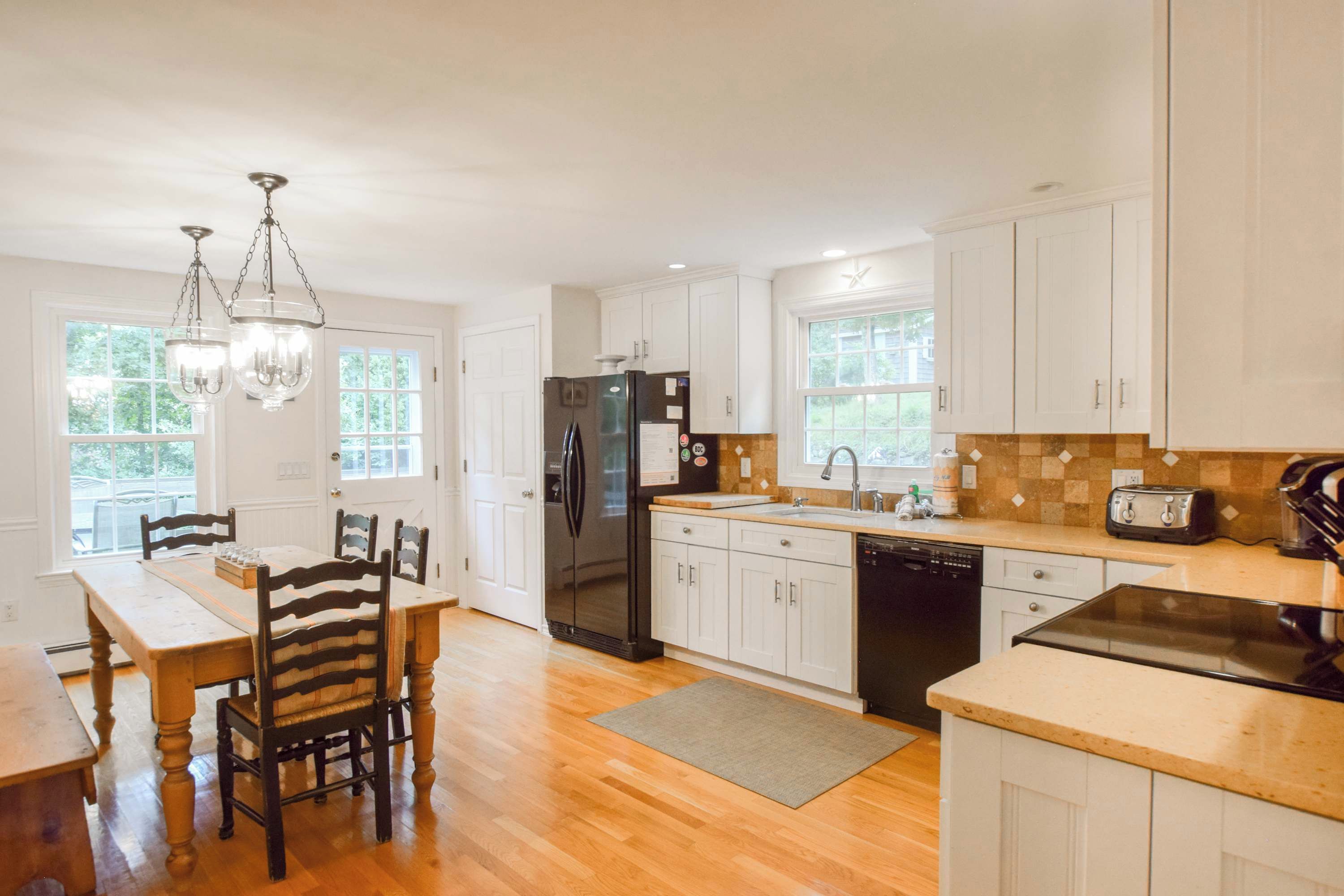 A kitchen with white cabinets, a black refrigerator, a wooden dining table with chairs, and a chandelier.