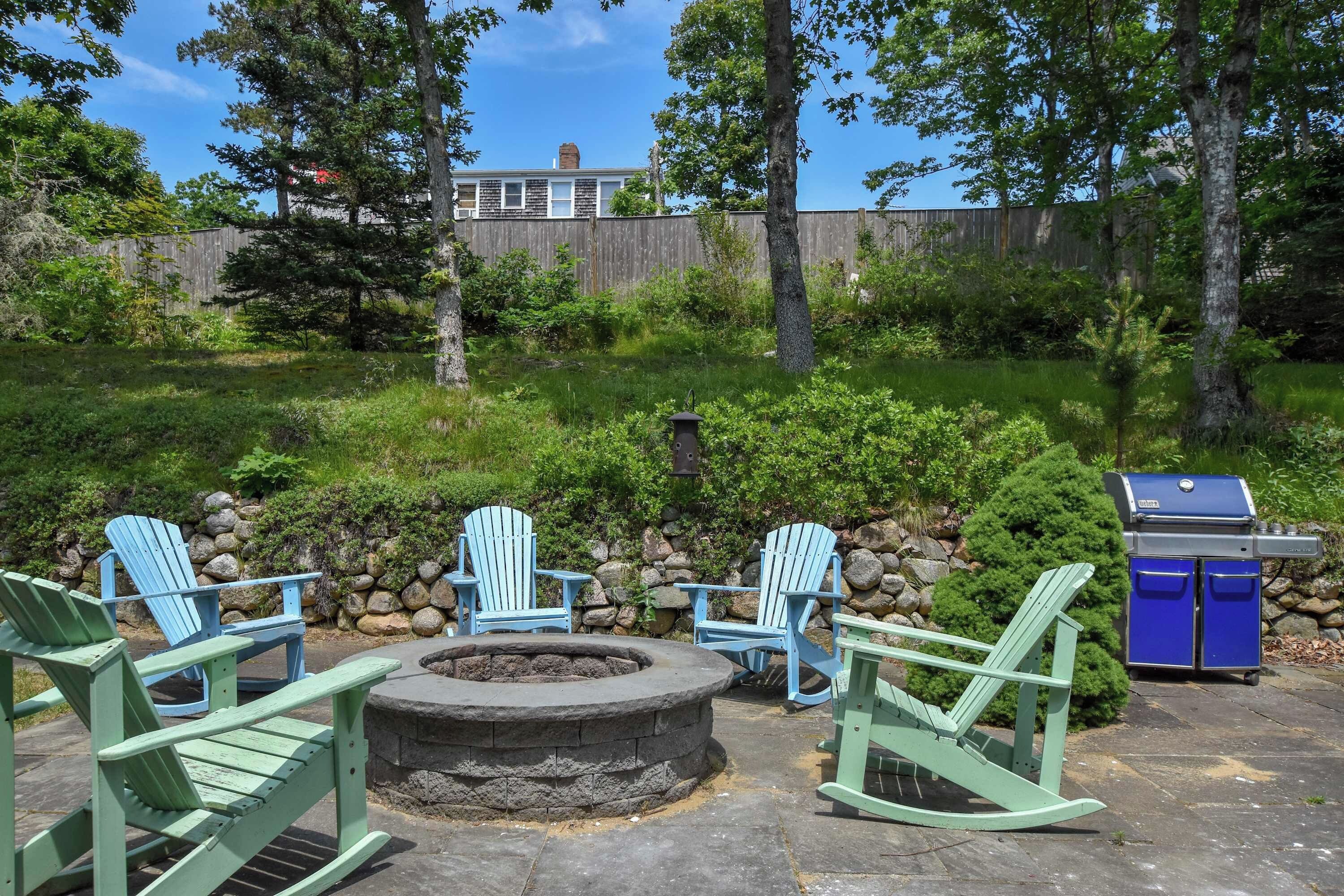 Un espace extérieur aménagé avec des chaises Adirondack, un foyer en pierre et un barbecue.