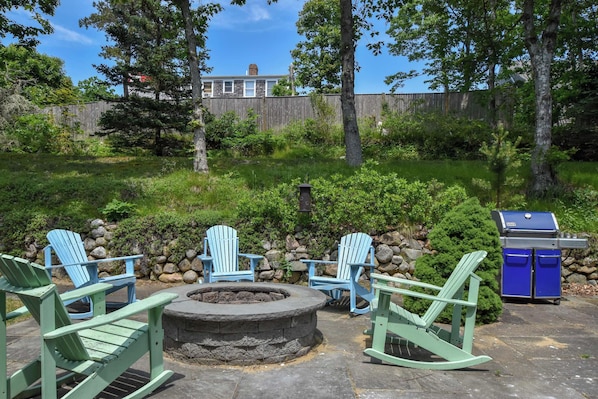 A patio area with Adirondack chairs, a stone fire pit, and a grill.