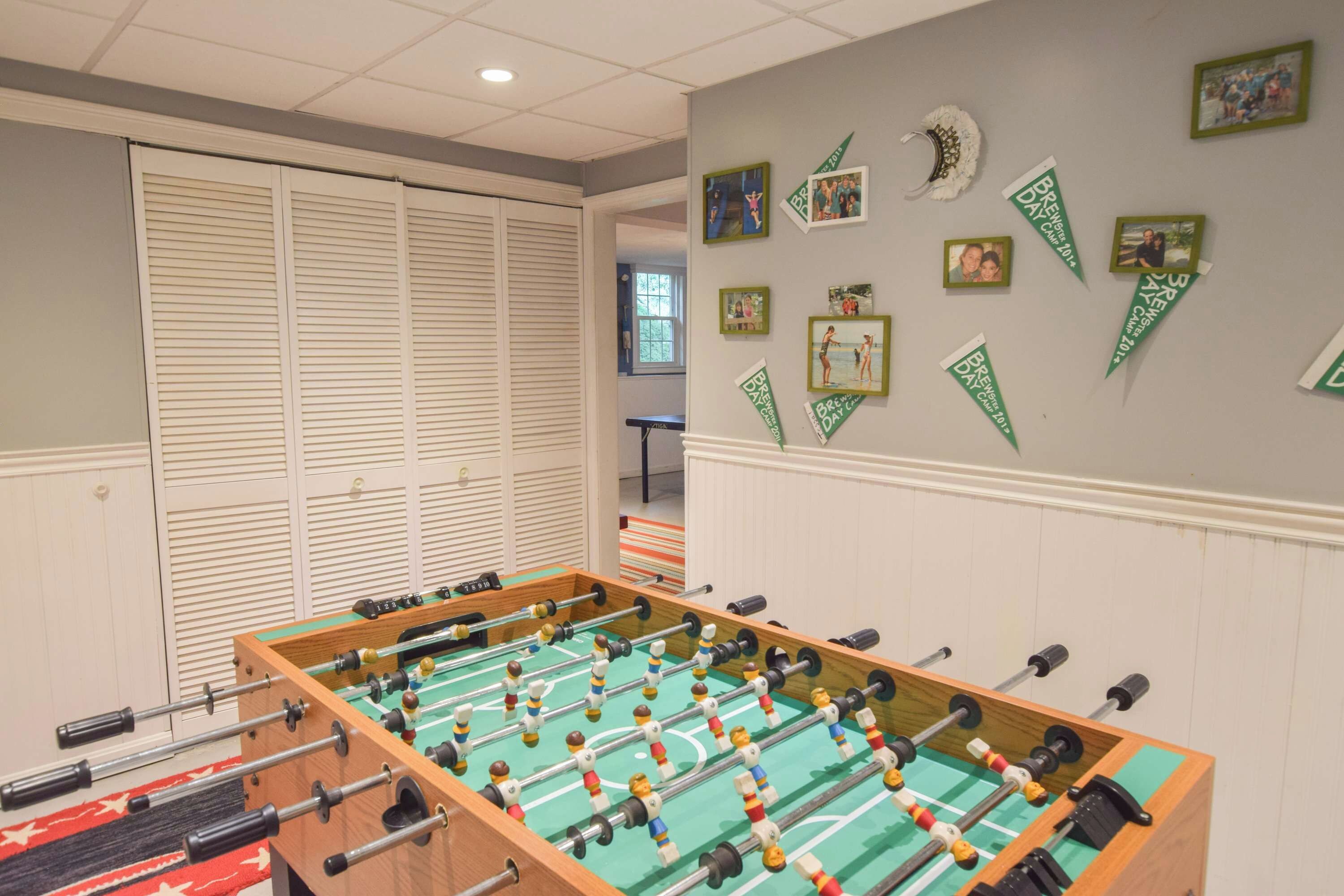 Une pièce avec une table de baby-foot, une fenêtre avec des stores et un mur décoré de photos et de banderoles.