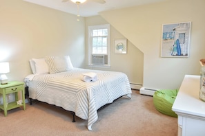 A bedroom with a bed, a nightstand, a green chair, a window, and a painting on the wall.