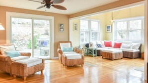 A spacious living room with wicker furniture, large windows, and a ceiling fan. - Spacious w/ Large Outdoor Area Fire Pit! (Chatham)