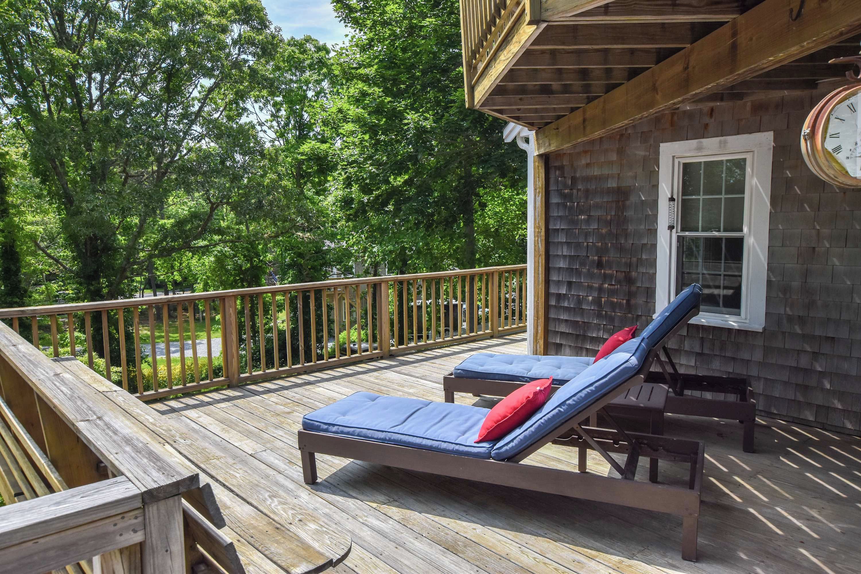 Une terrasse en bois avec deux chaises longues et une petite table, offrant une vue sur un paysage verdoyant et luxuriant.