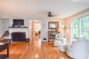 A spacious living room with hardwood flooring, a fireplace, a television, and a large window offering a view of the outdoors.