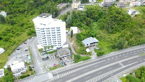 Vue aérienne d’un hôtel à plusieurs étages, doté d’un parking, entouré de verdure et situé à proximité d’une route à plusieurs voies.