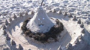 Un castillo de arena con un pico cónico y una base circular, rodeado por un foso de arena.