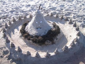 Ett sandslott med en konformad topp och en cirkelformig bas, omgivet av en vallgrav fylld med sand.