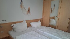 Una cama bien hecha con ropa blanca, cabecera de madera y mesita de noche con lámpara.